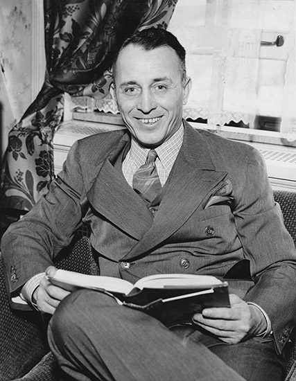 White man in suit sitting and smiling with open book in his lap