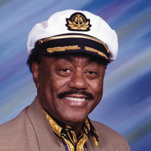 African-American man with mustache smiling in suit with naval cap