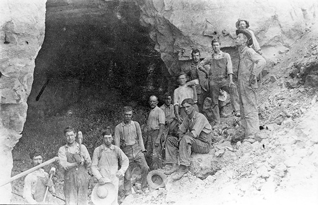 Group of white miners with tools before quarried side of a hill