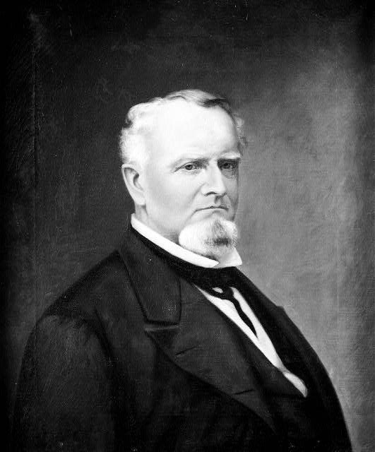 White man with white hair and beard in suit and tie