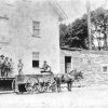 White men in hats outside multilevel warehouse with horse drawn wagon