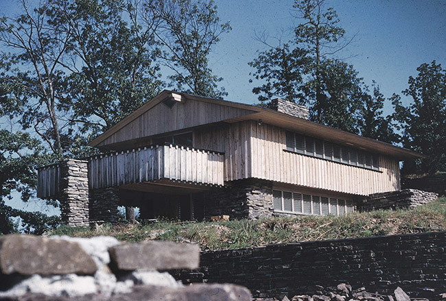 Multistory house with covered porch and balcony on hill with brick wall in the foreground