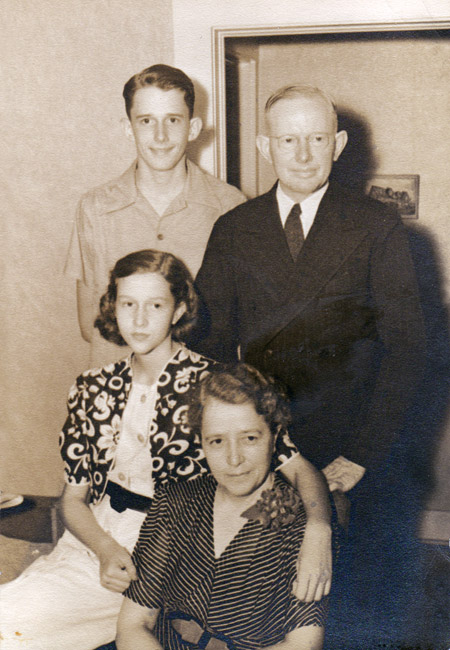 Portrait of white family with son and father standing behind seated girl who has her arm around seated mother