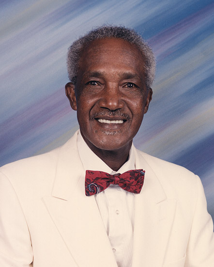 African-American man with mustache smiling in white suit with red bow tie