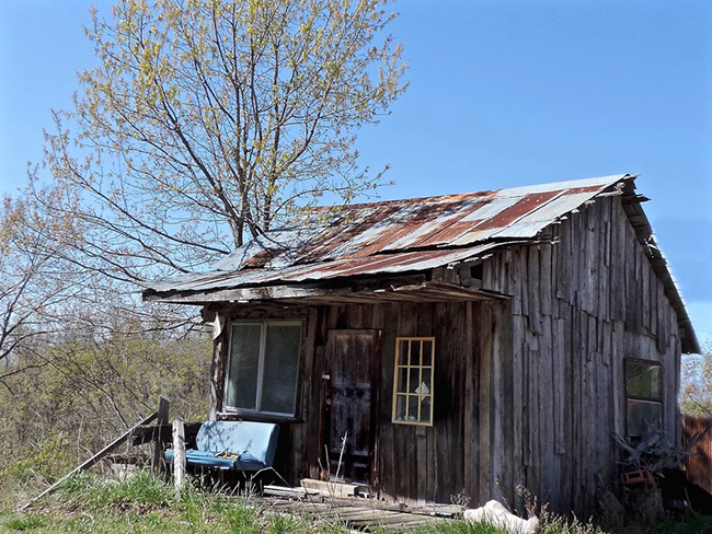 Abandoned shop building with rusted metal roof and couch on covered porch