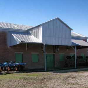 Brick building with sheet metal awning and agricultural equipment in front yard