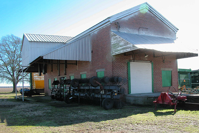 Side view of brick building with sheet metal awning and agricultural equipment in front yard