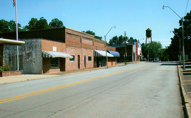 Brick storefronts on two-lane street with water tower in the background