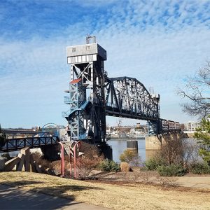 Steel arch foot bridge over river with elevator and stairs and small walking bridge leading up to it
