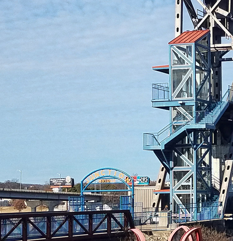 Close-up of entrance to steel arch walking bridge with elevator and stairs
