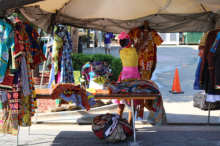 African-American woman hanging up multicolored clothing in a tent with table