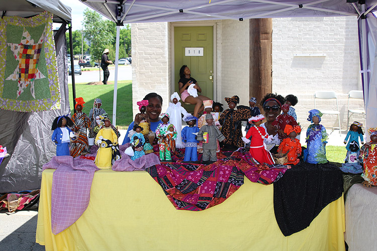 African-American women selling handmade dolls under tent canopy