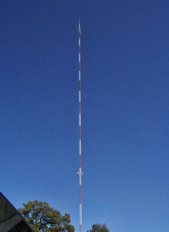 Red and white radio tower against blue skies