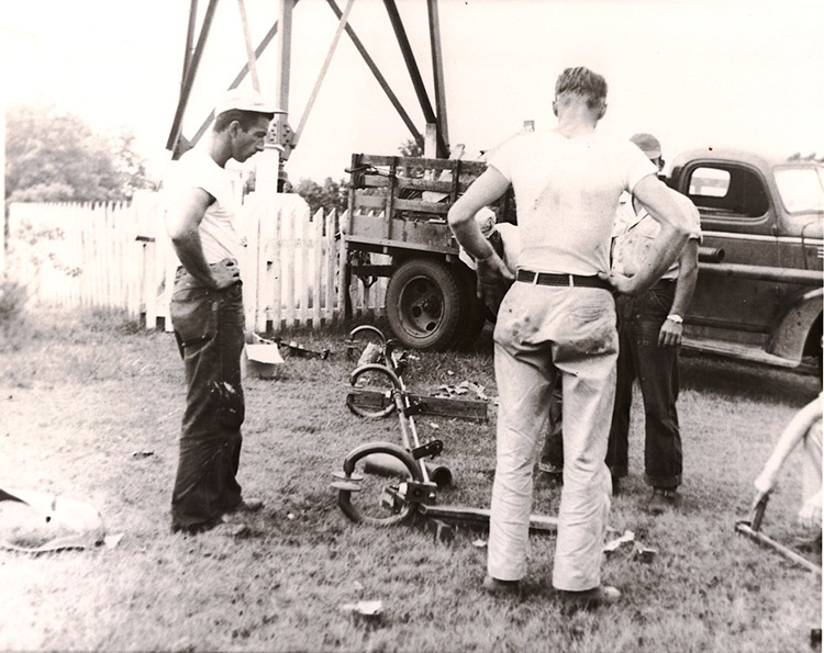 Three white men at bottom of radio tower with truck at work
