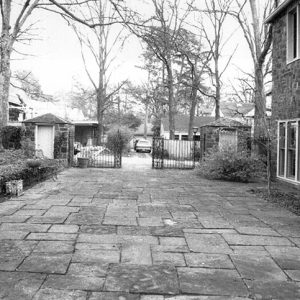 Stone driveway and double gates outside multistory brick house with gate houses on either end under bare trees
