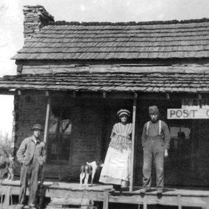White men woman and dogs on covered porch of single-story building