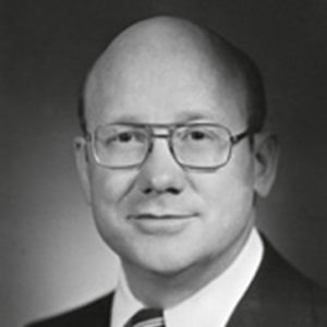 Bald white man with glasses smiling in suit and tie