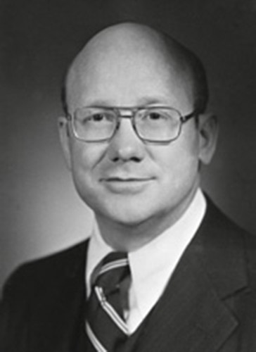 Bald white man with glasses smiling in suit and tie