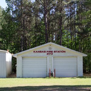 Single garage building next to two-bay garage building with red lettering on grass with trees behind them