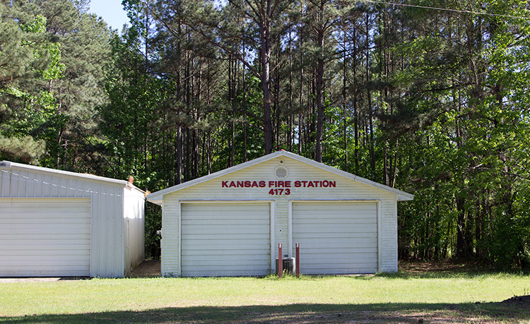 Single garage building next to two-bay garage building with red lettering on grass with trees behind them