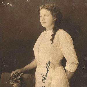 Young African-American woman standing in white dress with flowers in her right hand resting on back of a chair