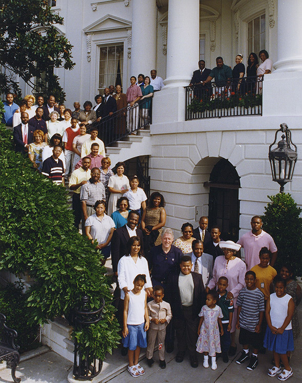 large African-American family posing with white man on staircase of multistory building with arched windows and white paint