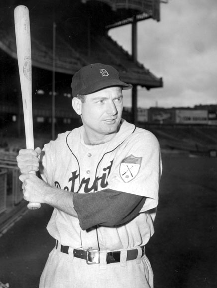 White man holding a bat in Detroit Tigers uniform with empty stadium in background