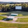 Vacant drive-in theater in sunshine with screen buildings and driveways and rolling hills in background
