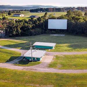 Vacant drive-in theater in sunshine with screen buildings and driveways and rolling hills in background