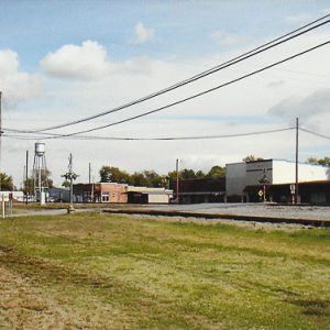 Street with buildings and expanse of grass with water tower in the distance