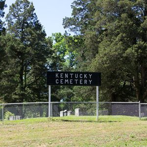 Fenced-in cemetery with "Kentucky Cemetery" sign and trees in the background