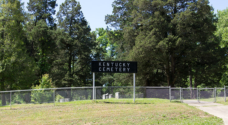 Fenced-in cemetery with "Kentucky Cemetery" sign and trees in the background