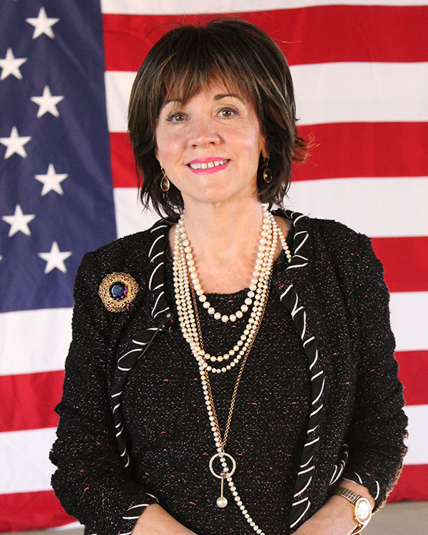 White woman smiling with American flag in the background