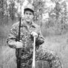 White man wearing camouflage and holding baseball bat and shotgun
