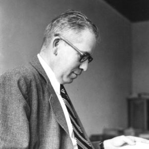 White man wearing glasses in suit and tie reading a piece of paper