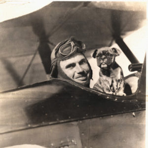 white man in aviation goggles with dog pose in biplane