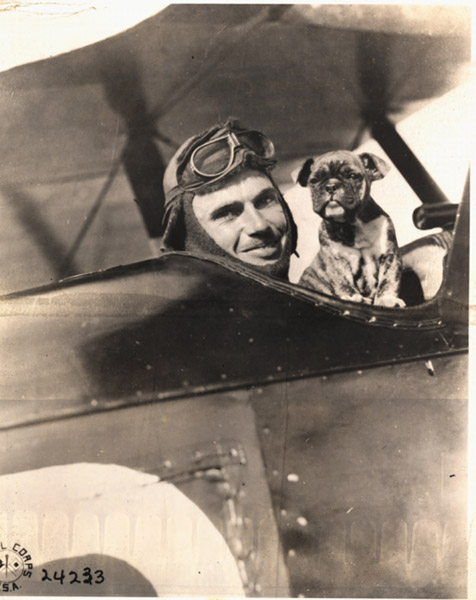 white man in aviation goggles with dog pose in biplane