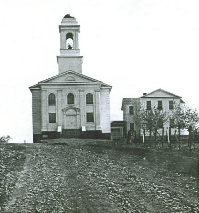 Two-story church building with bell tower attached to two-story school house