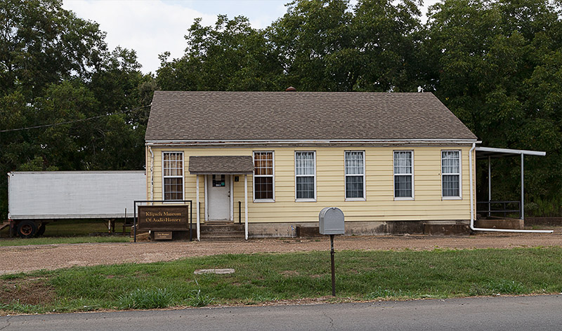 Single-story building with yellow siding and semi trailer behind it