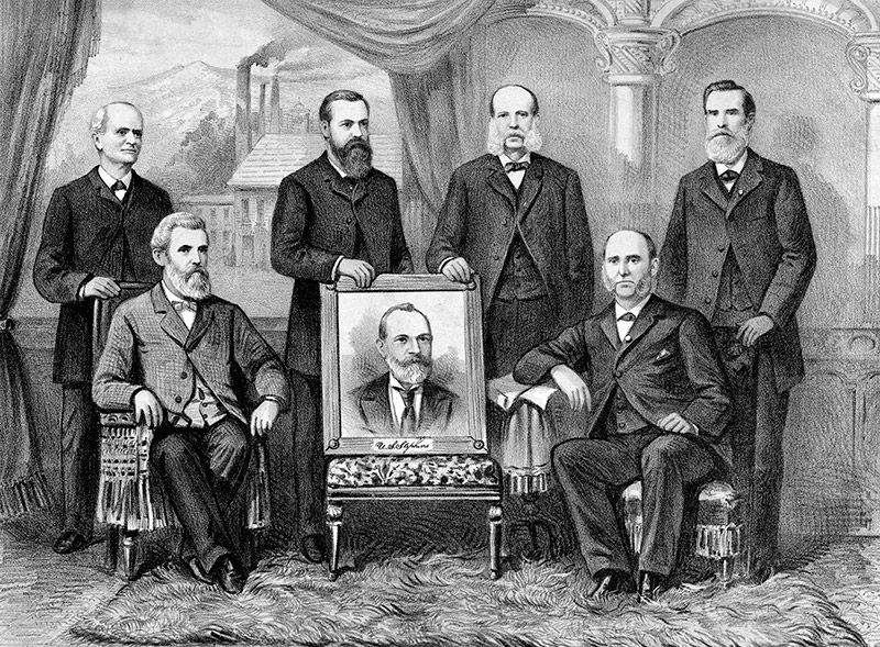 Group of white men in suits with portrait of white man in suit