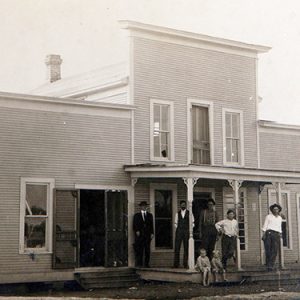 Group of white men woman and children outside two-story building
