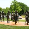 Group of nine bronze sculptures depicting male and female high school students carrying books on concrete pad on lawn