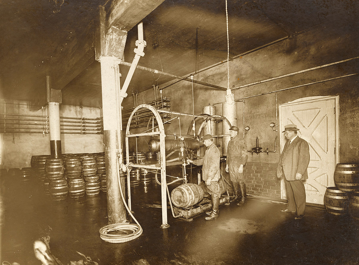 Three white men in brewery with barrels and machinery