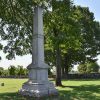 Tall stone obelisk with pedestal under two trees in cemetery