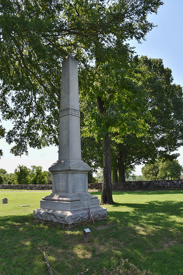 Tall stone obelisk with pedestal under two trees in cemetery