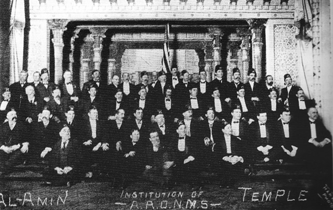 Group of white men in formal suits and hats inside temple building