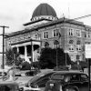 Three-story courthouse with columned front and dome and street with parked cars