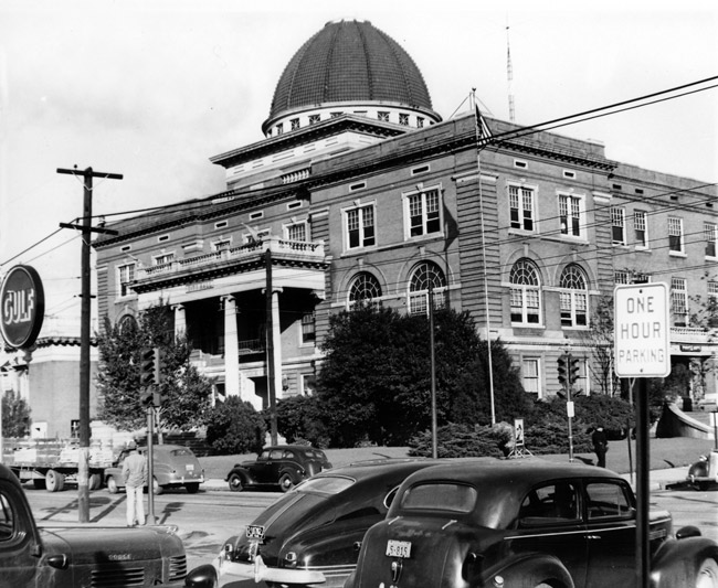 Three-story courthouse with columned front and dome and street with parked cars