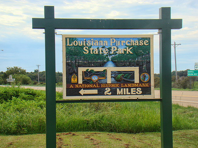 Wooden sign for "Louisiana State Park" in grass next to highway