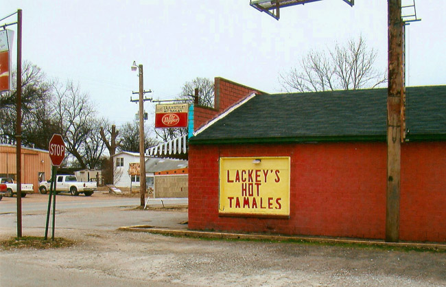 Side view of single-story brick building on town street corner with "Lackey's Hot Tamales" sign on its side